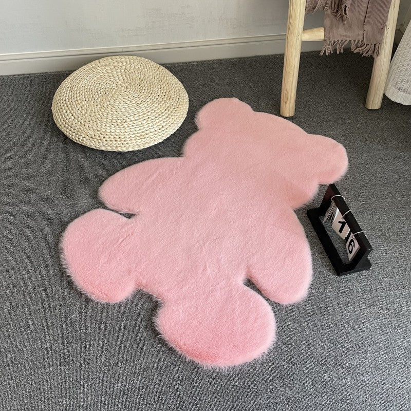Pink teddy bear-shaped rug on a gray floor with a woven basket and wooden stool in the background.