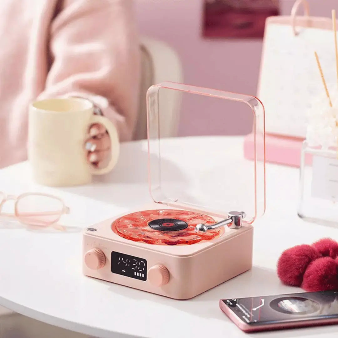Pink record player on a table with a cup and phone in the background
