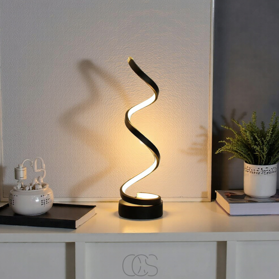 Modern black table lamp with wavy design on a white surface, casting a shadow on a light-colored wall.