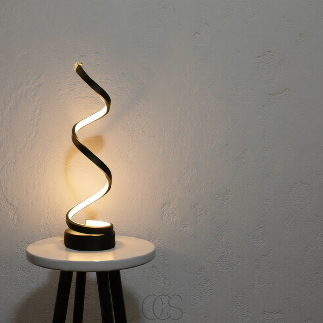 Modern table lamp with a wavy design on a white pedestal against a gray wall.