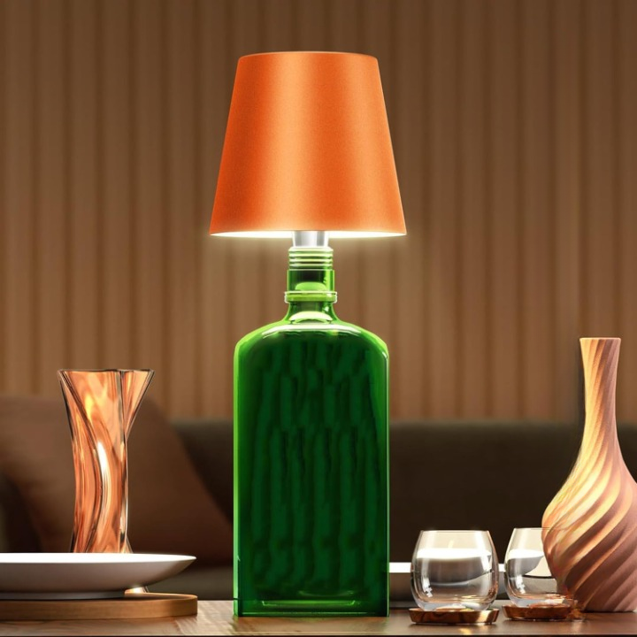 Green bottle repurposed as a lamp with an orange shade on a table.