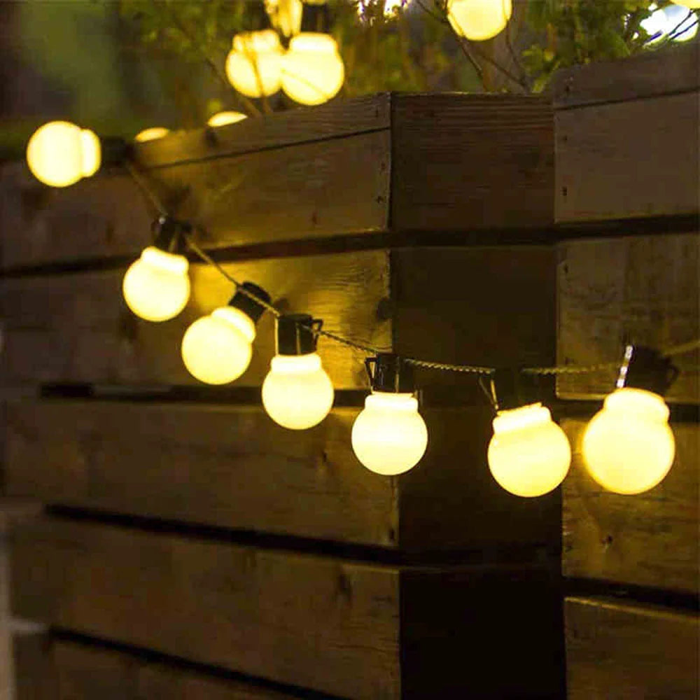 String of illuminated light bulbs hanging against a wooden fence