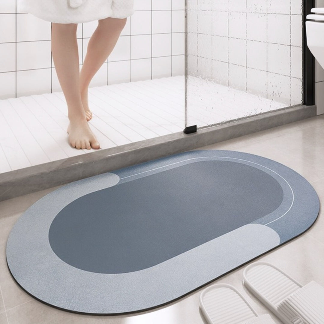 Oval bath mat on a bathroom floor with a glass shower door in the background.