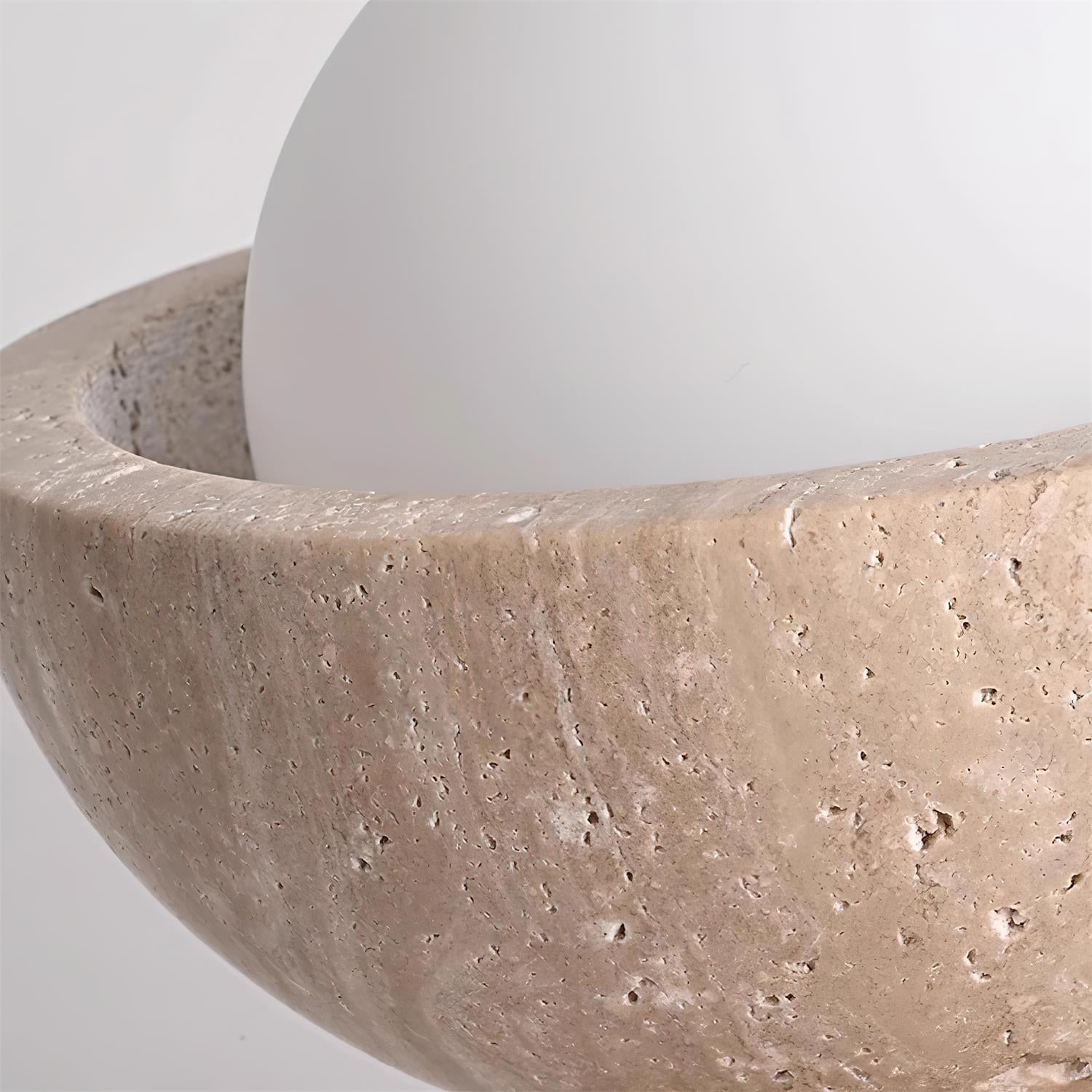 Close-up of a textured stone bowl with a white sphere inside on a light gray background