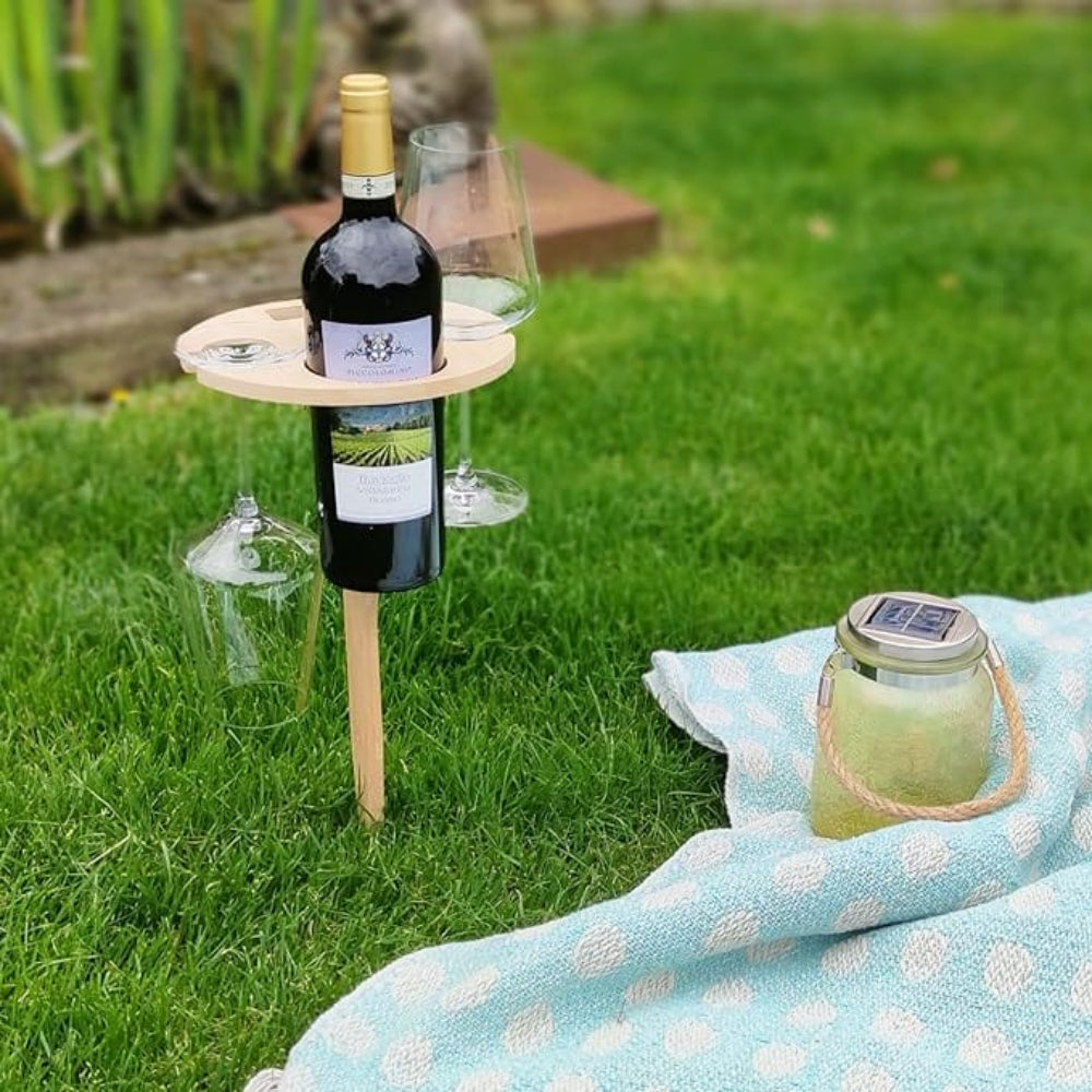 Wine bottle on a stand with glasses and a candle on a picnic blanket in a grassy area