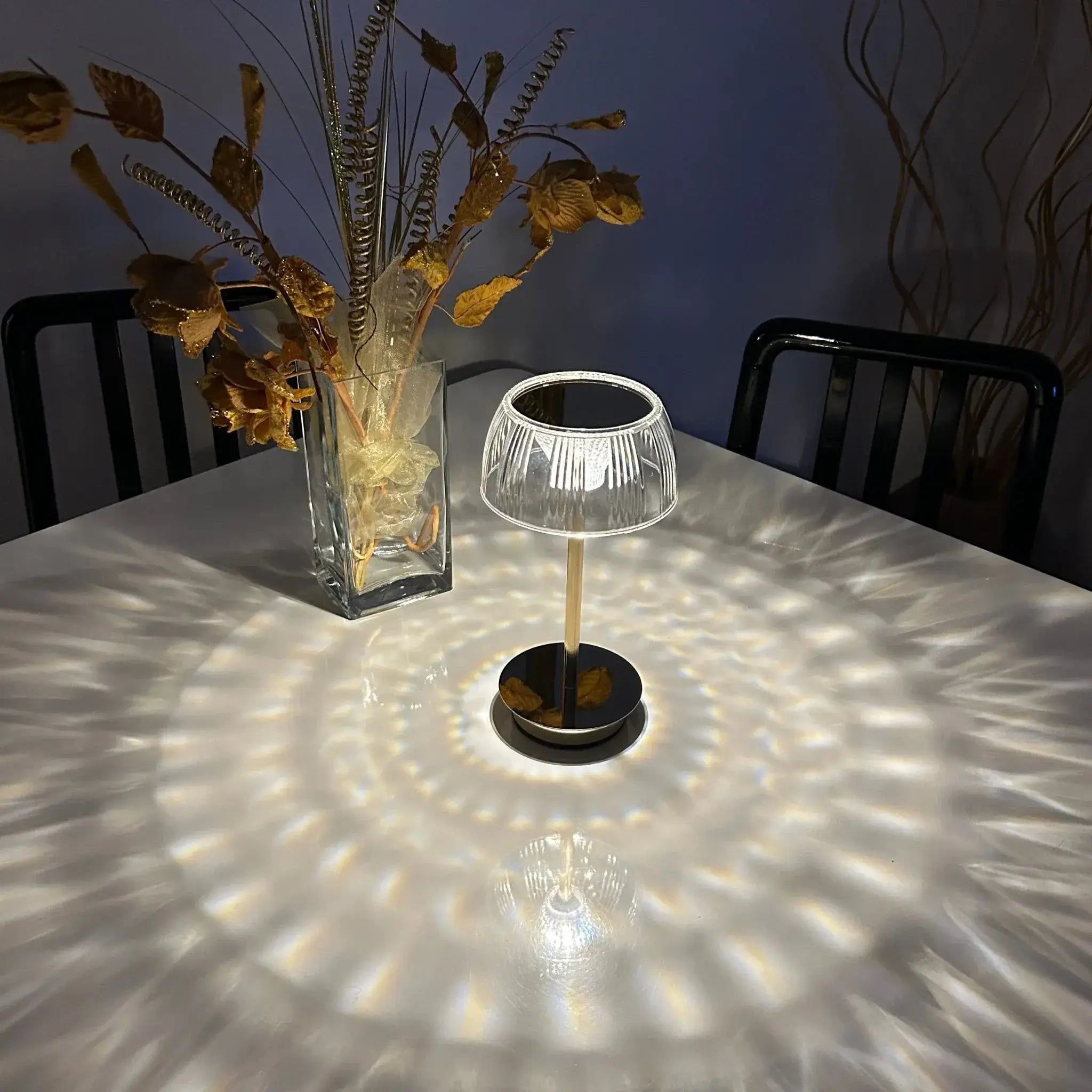 Small table lamp casting a pattern on a table with a vase of dried flowers in the background.