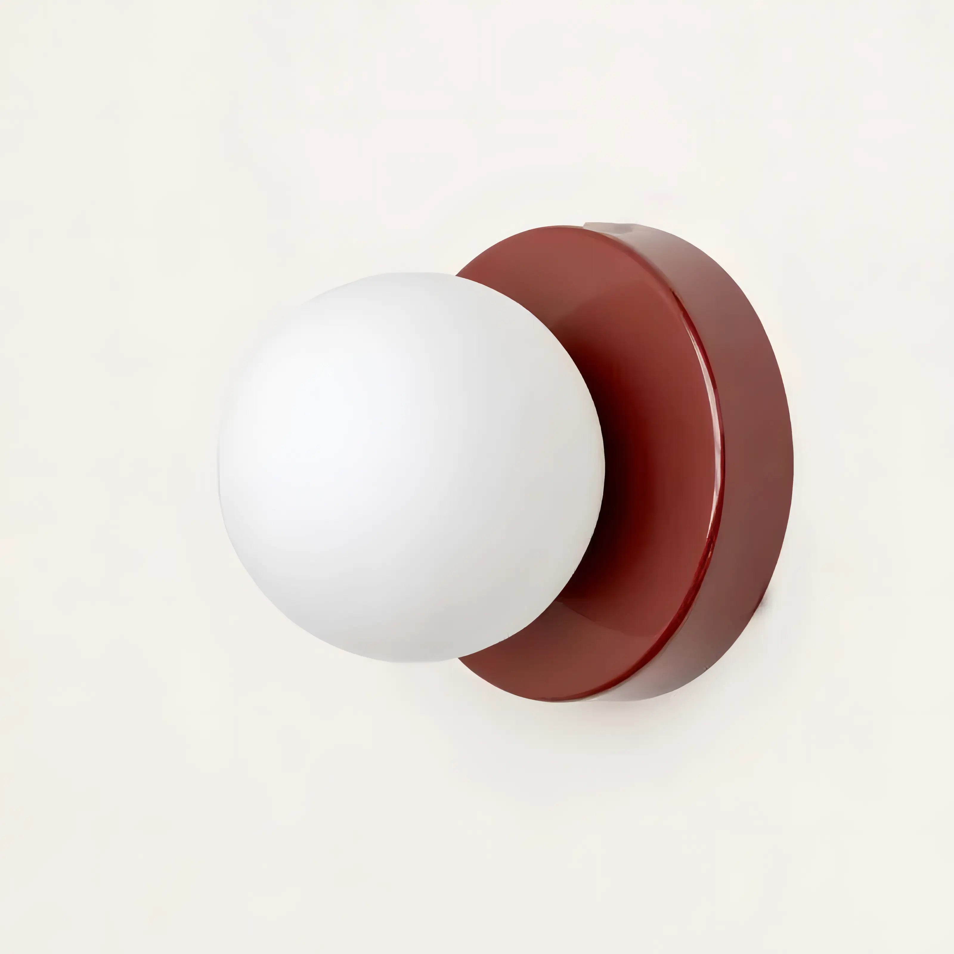 Wall sconce with white globe light and red finish on a white background
