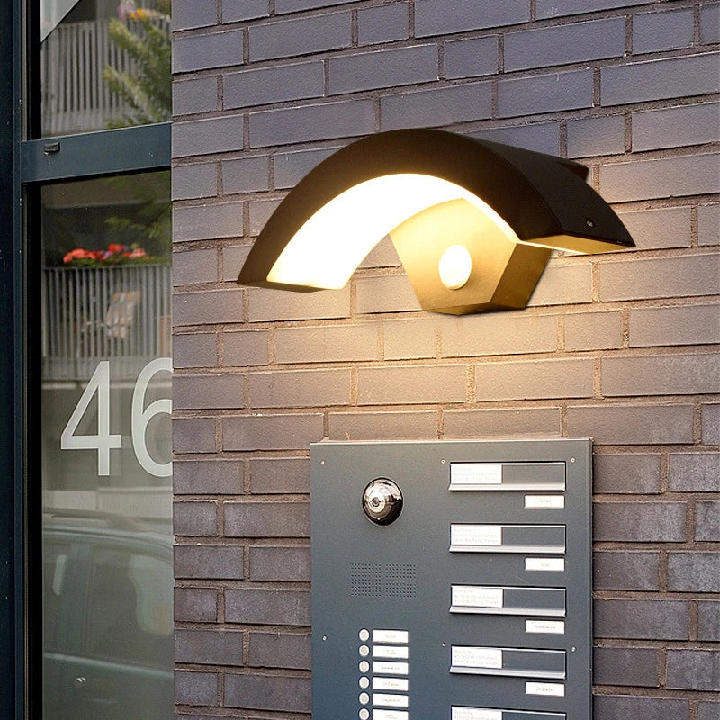Modern outdoor wall light fixture on a brick wall with a door buzzer unit below.
