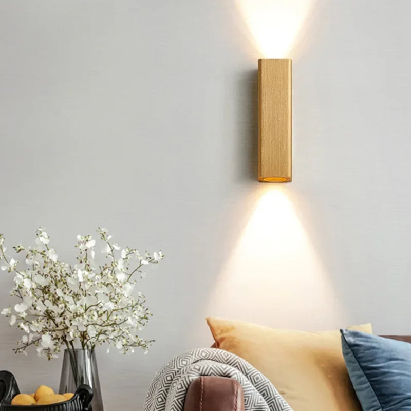 Wall-mounted light fixture on a gray wall with a vase of flowers and pillows on a couch.