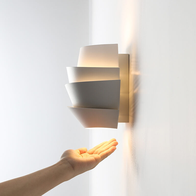 Modern wall sconce with a hand reaching towards it on a light gray background
