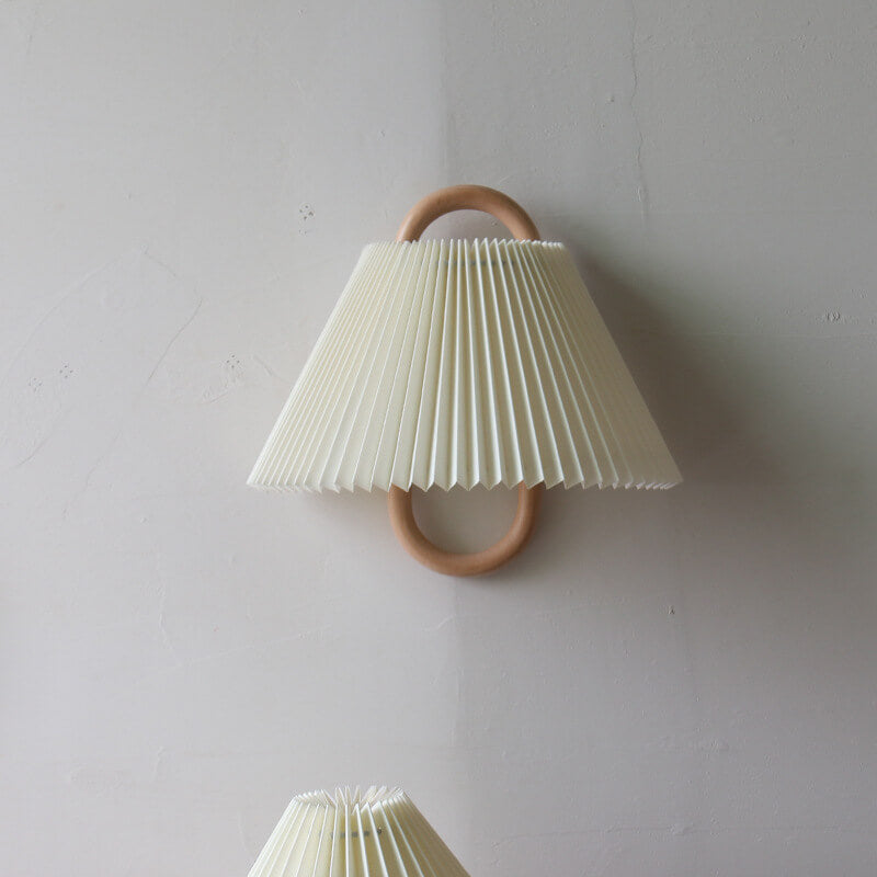 Wall-mounted pleated lamp with wooden ring on a light gray wall