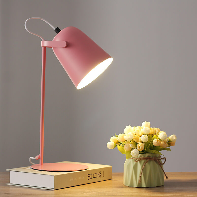 Pink desk lamp on a wooden surface with a small potted plant against a gray background