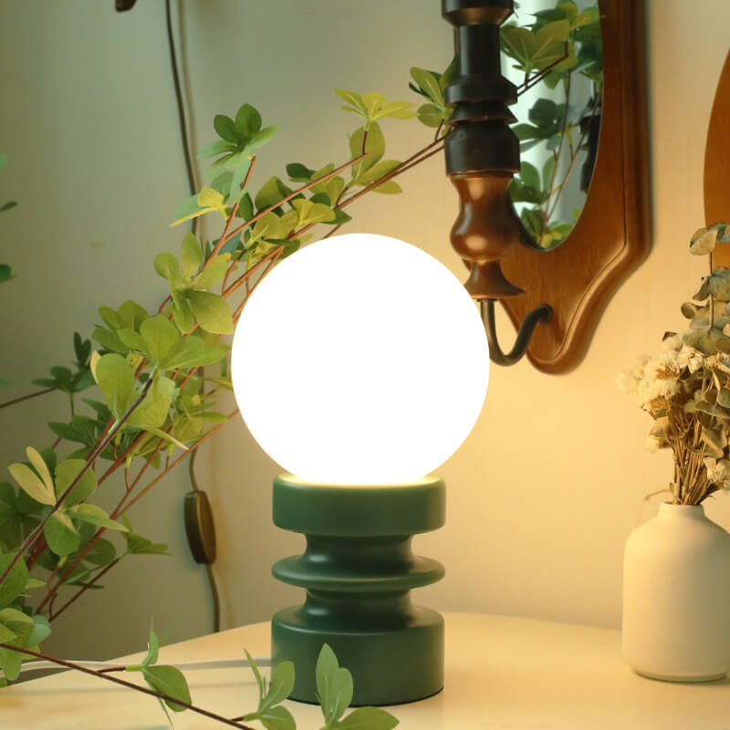 White light bulb on a green base with plants and a mirror in the background