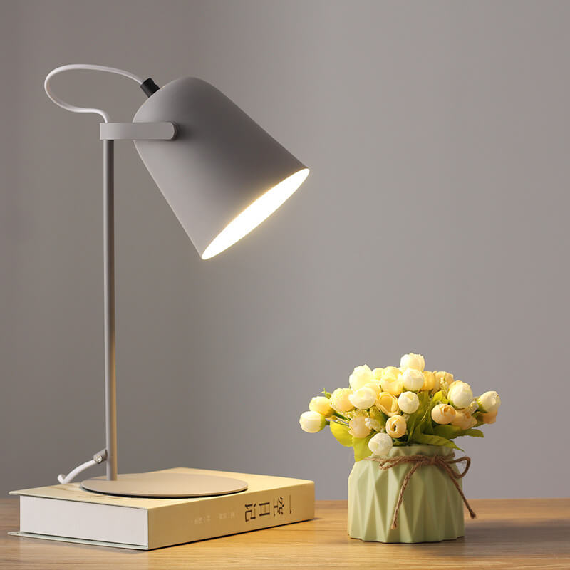 Desk lamp on a book next to a small potted plant on a wooden surface with a gray background