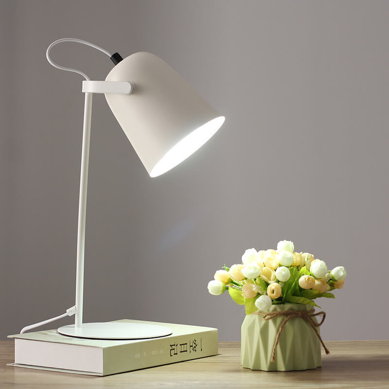White desk lamp on a book next to a small vase with flowers on a wooden surface.