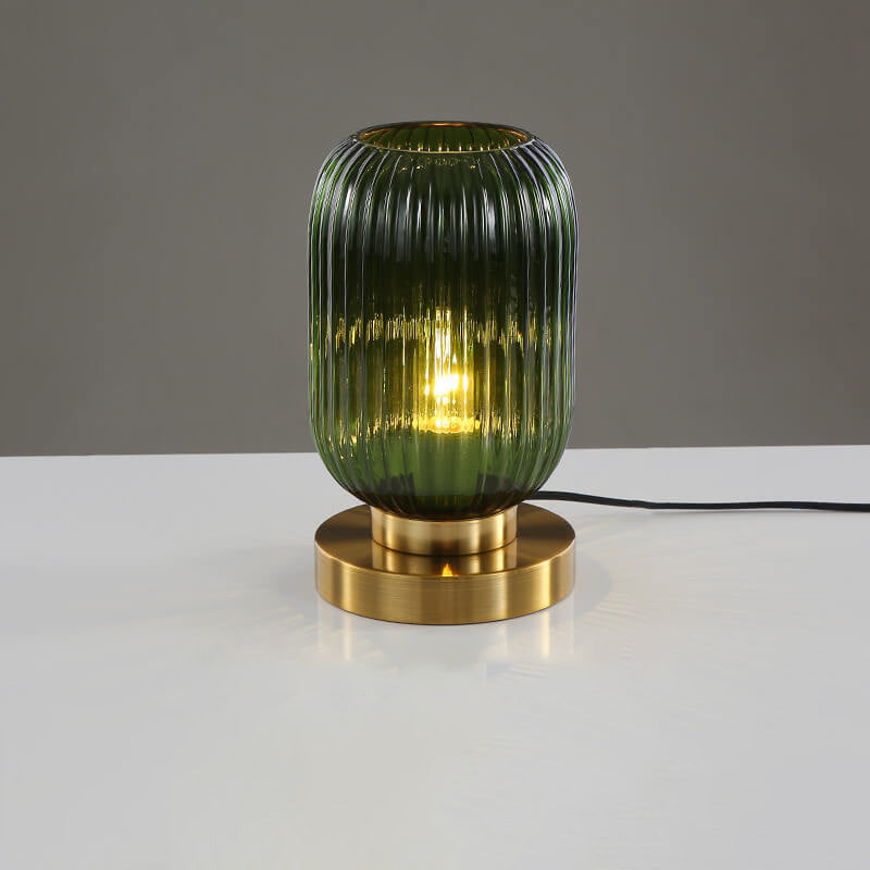 Green glass table lamp with gold base on a white surface and gray background
