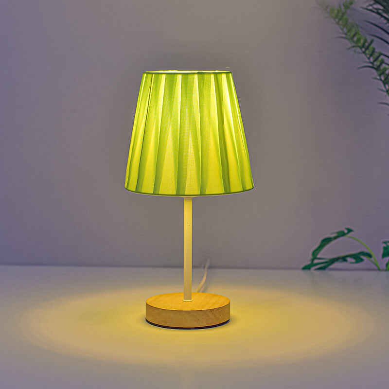 Table lamp with a green pleated shade and wooden base on a neutral background