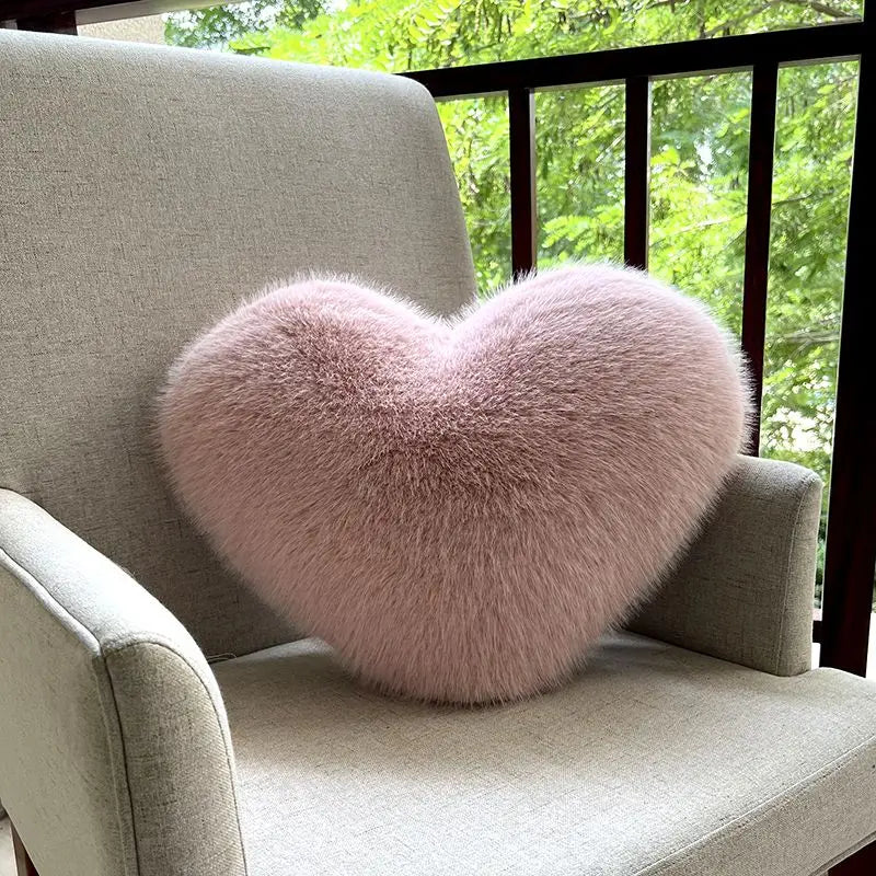 Heart-shaped fluffy pink pillow on a beige chair with a blurred green outdoor background