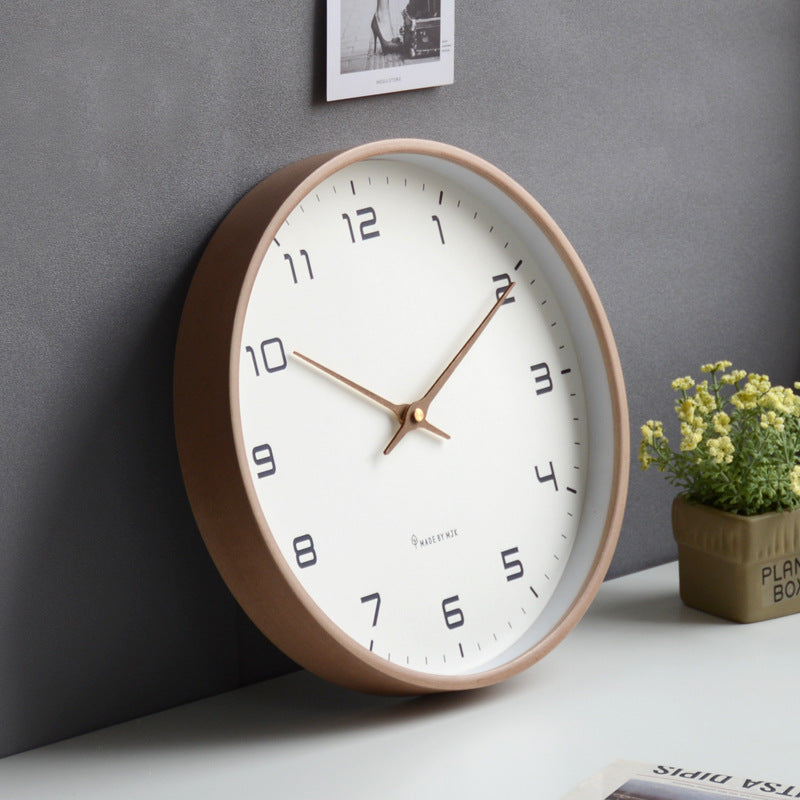 Wall clock with a brown frame on a gray wall with a plant and photo frame in the background.