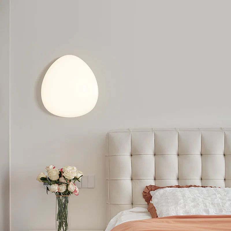 Round wall light fixture in a bedroom setting with a bed and flowers.