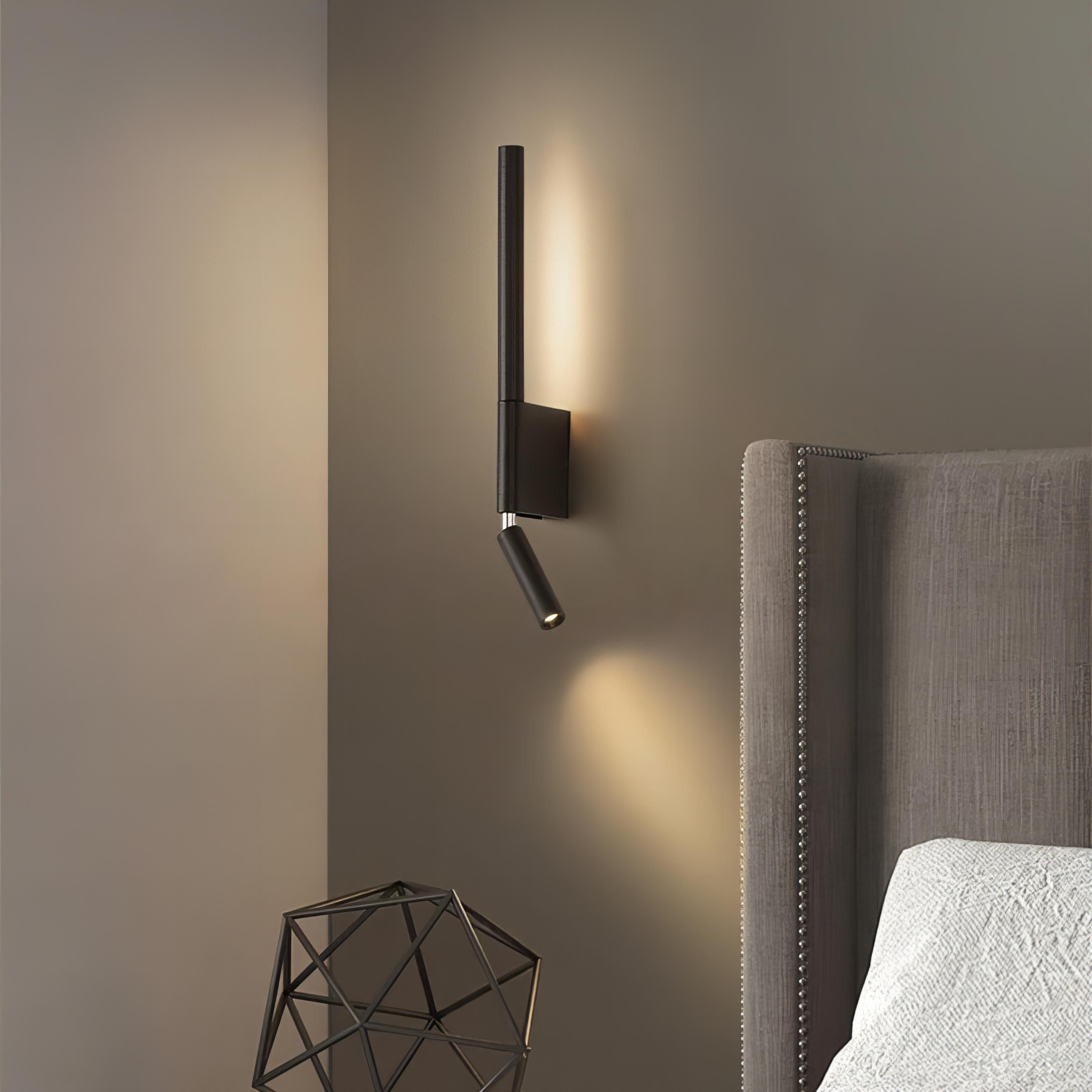 Modern wall-mounted light fixture on a gray wall next to a bed with a headboard.