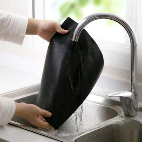 Person washing a black leather item under running water in a kitchen sink.