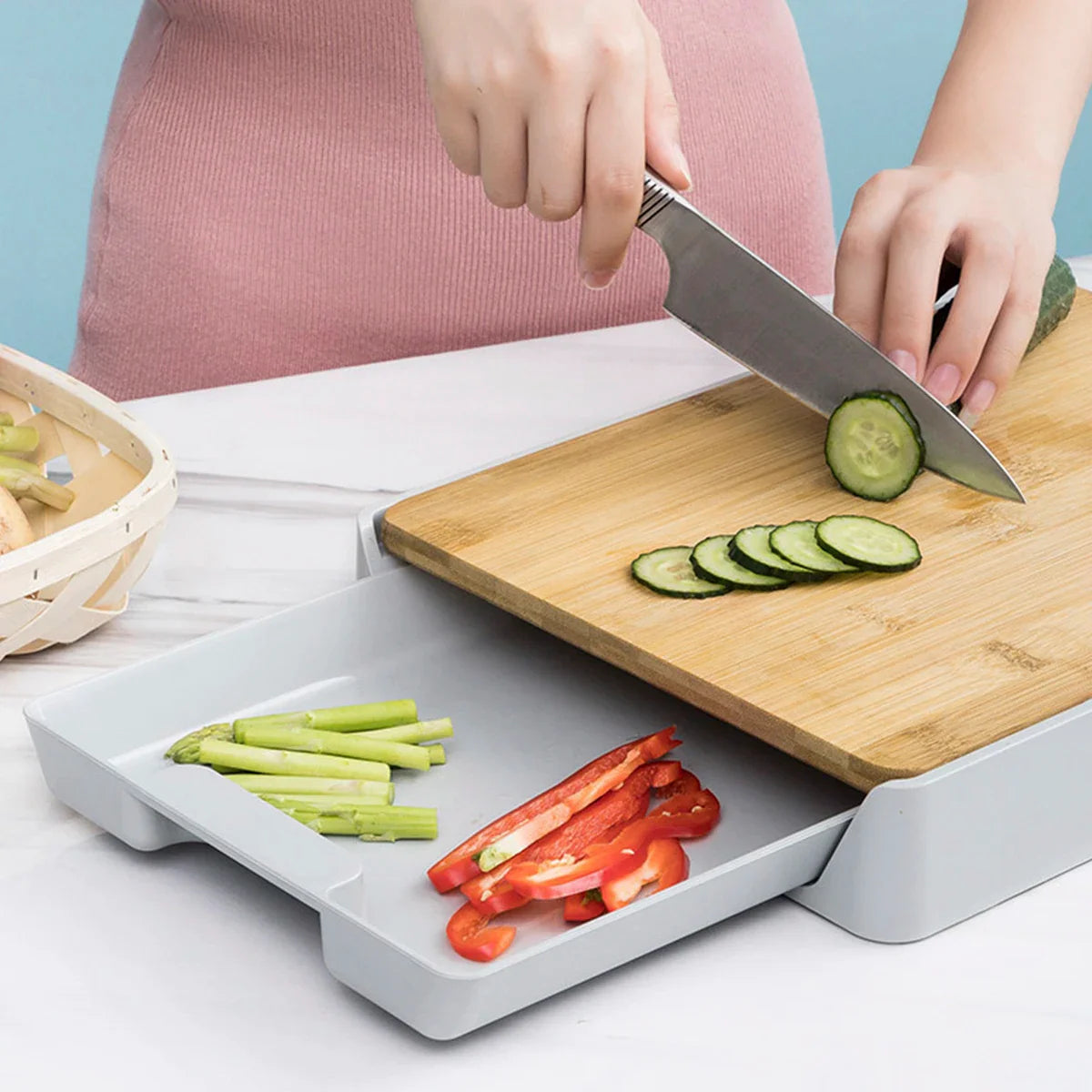 Person slicing cucumbers on a wooden cutting board with a knife, using a white cutting board holder to catch vegetable scraps.