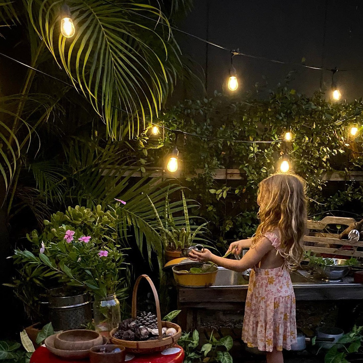 Child in a garden at night with string lights and plants