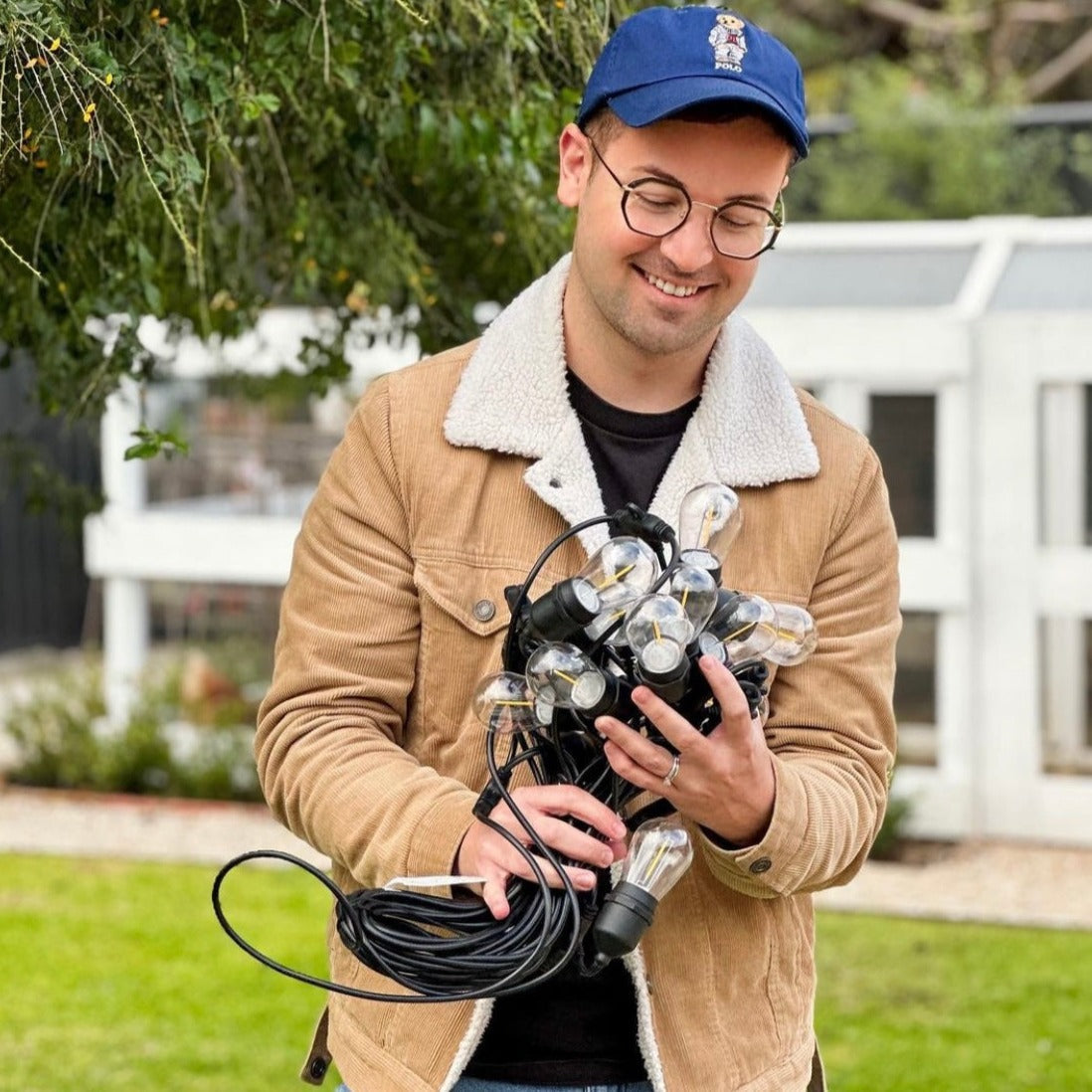 Man holding outdoor string lights and extension cord in a garden setting
