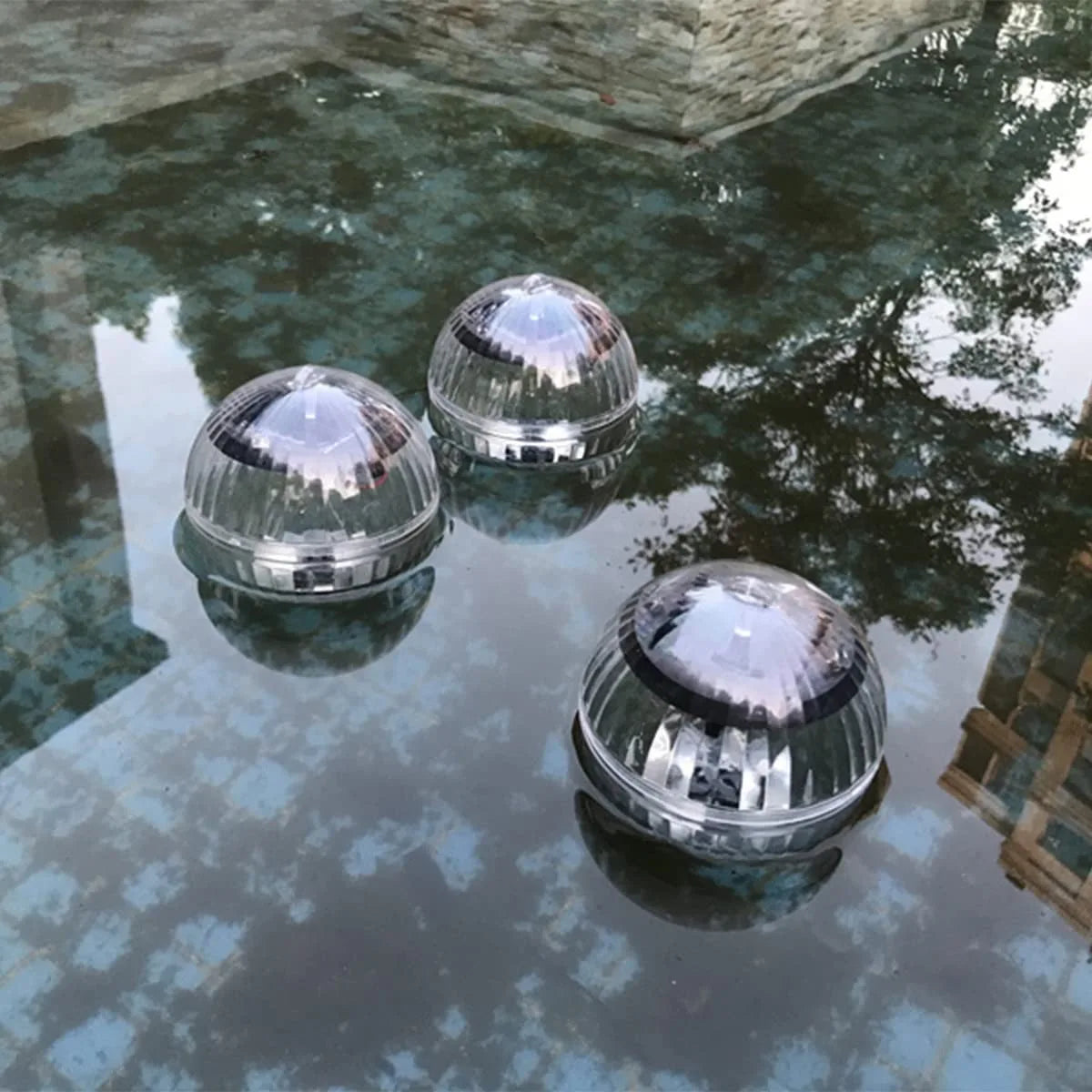 Three spherical floating lights on a pool surface with a stone wall in the background.