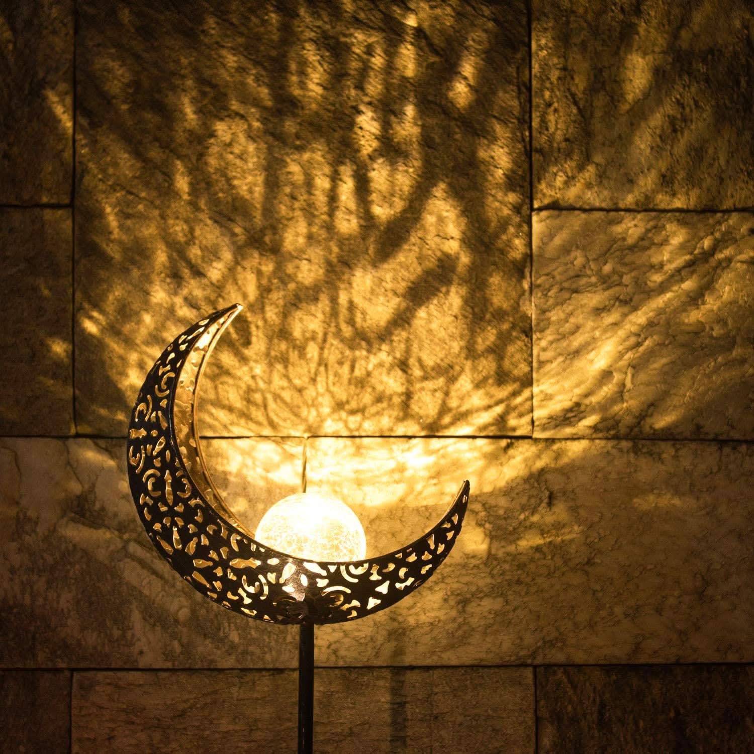 Decorative metal moon lamp casting a shadow on a textured wall.