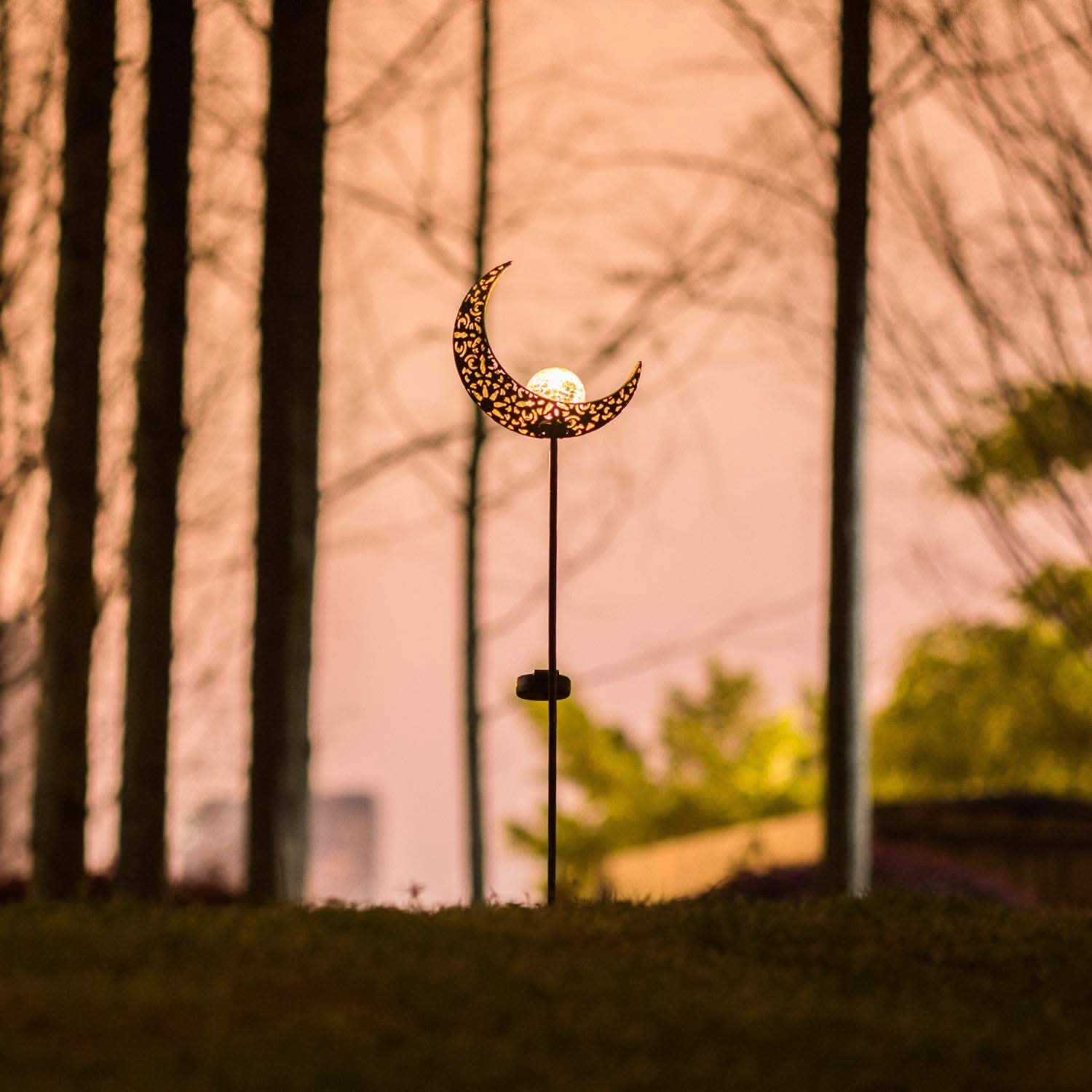 Decorative outdoor light shaped like a crescent moon with trees in the background