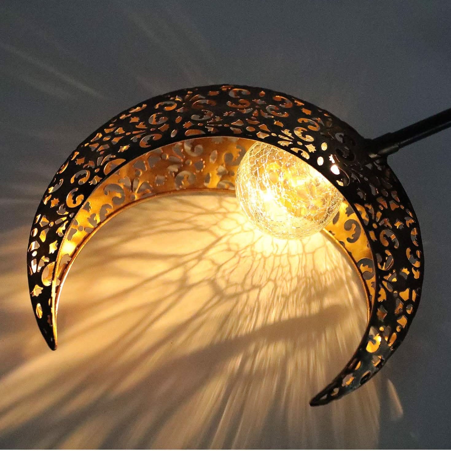 Decorative wall light shaped like a crescent moon with intricate patterns on a dark background.