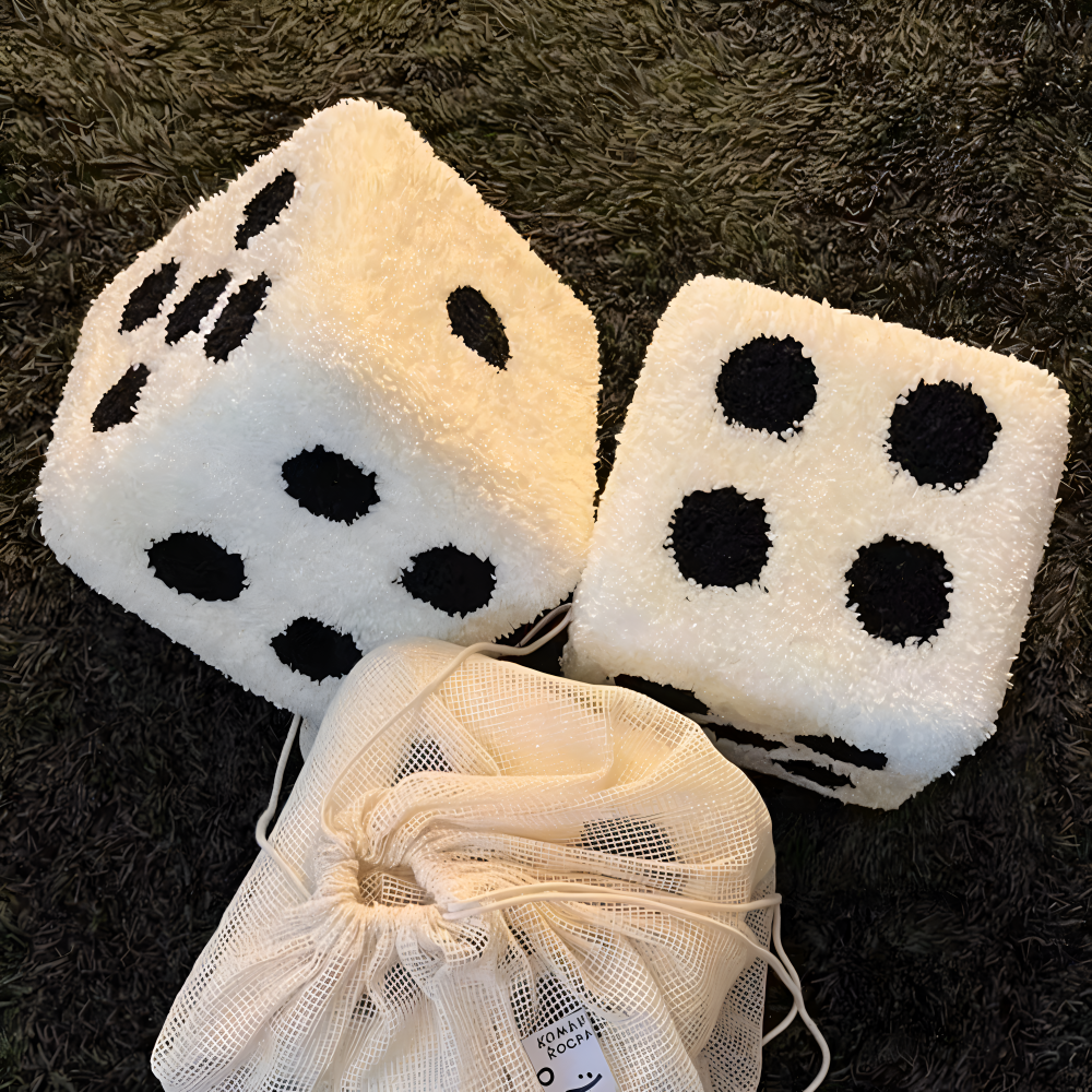 Two large white dice with black dots on a dark textured surface, accompanied by a drawstring bag.