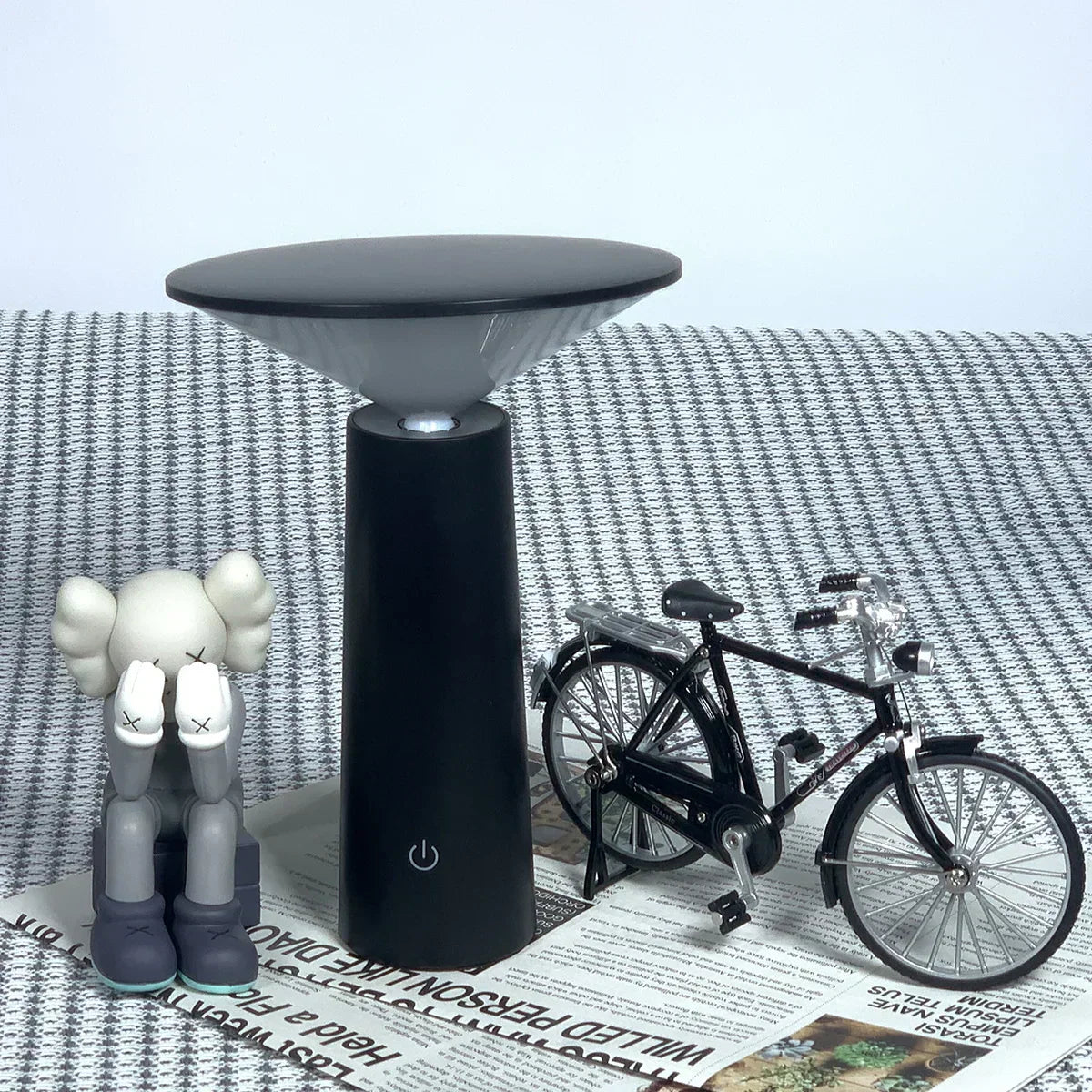 Black lamp with a small bicycle and toy figure on a textured surface