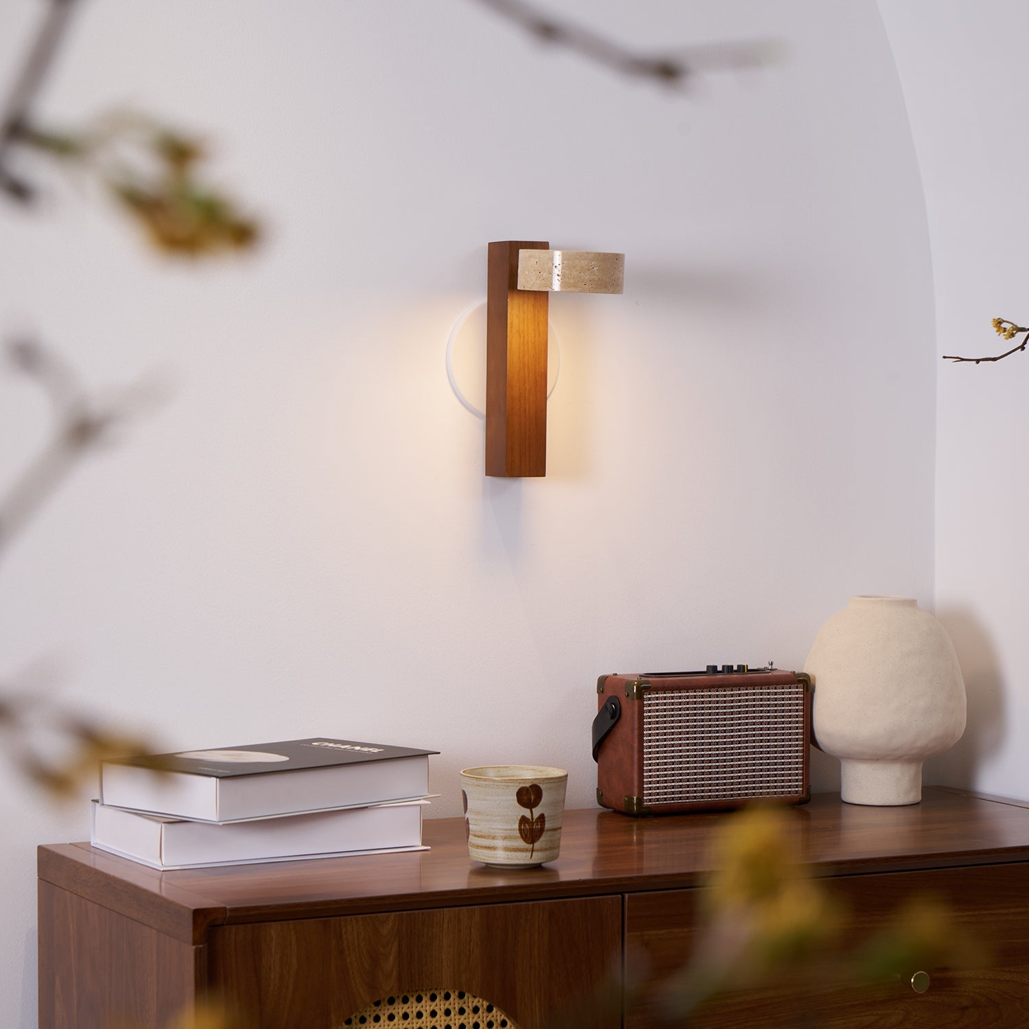 Wall-mounted light fixture on a wall above a wooden surface with books, a radio, and a vase.