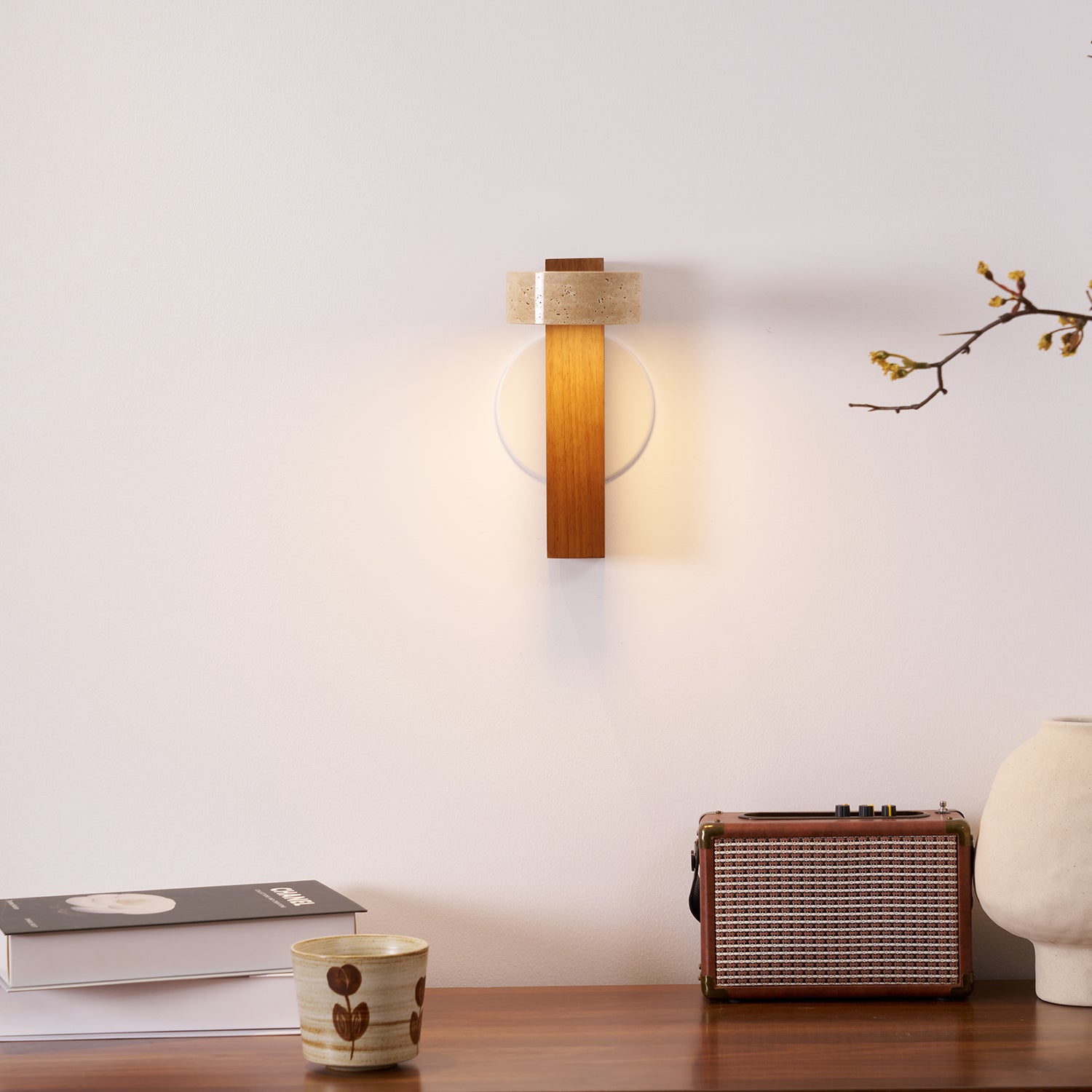 Wall-mounted light fixture on a wall with a table below featuring books, a cup, and a vintage radio.