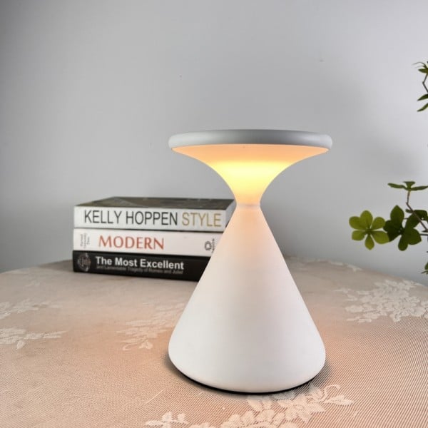 Conical table lamp on a surface with books and a plant in the background