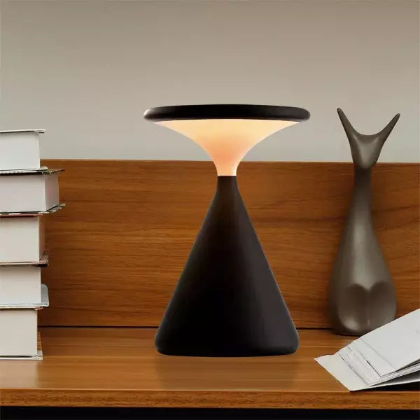 Black table lamp on a wooden surface with books and a decorative object in the background
