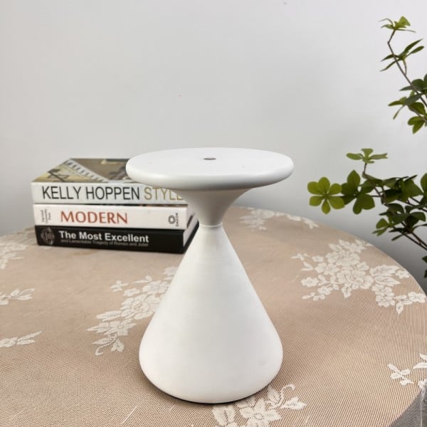 White ceramic stool on a table with books and a plant in the background