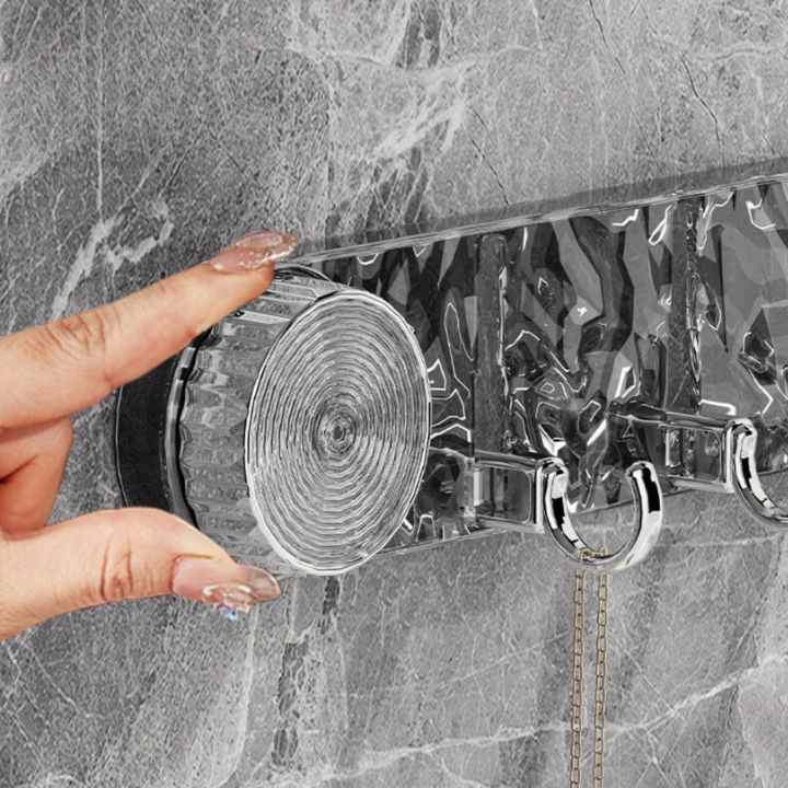 Hand holding a transparent plastic strip with metal hooks against a marble wall.
