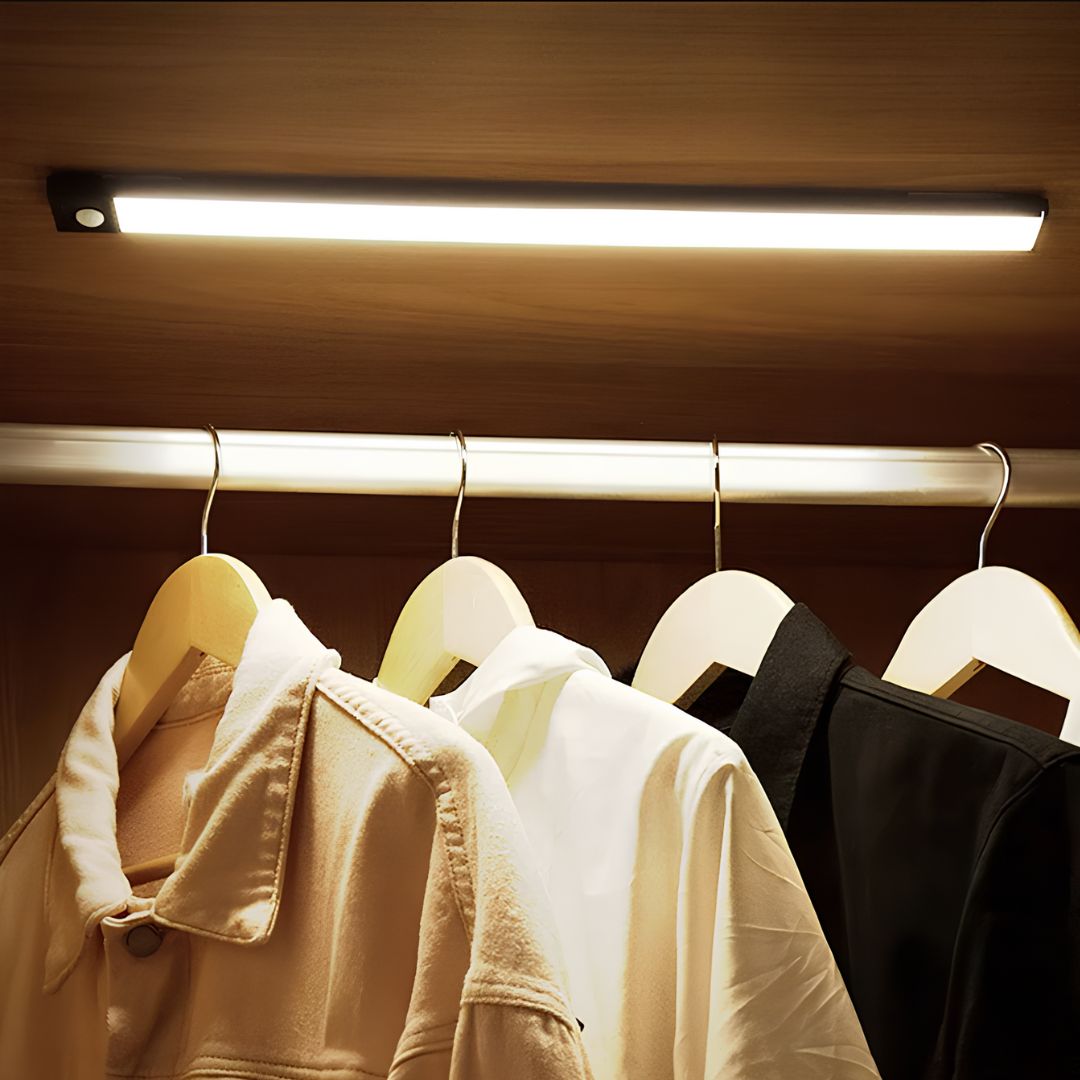 Clothing on hangers under a strip light in a closet