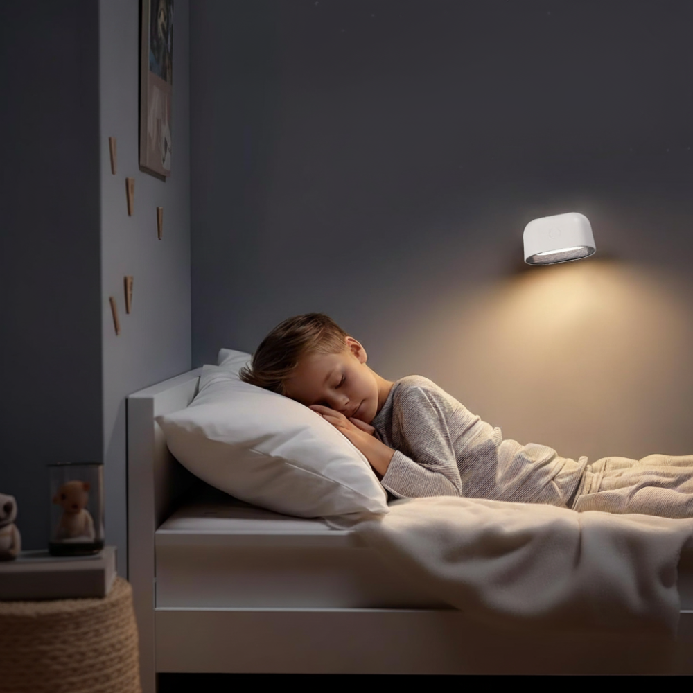 Child sleeping in a bed with a night light on the wall above.