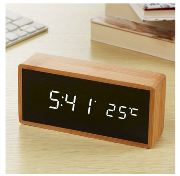 Digital clock with wooden frame displaying time and temperature on a desk.