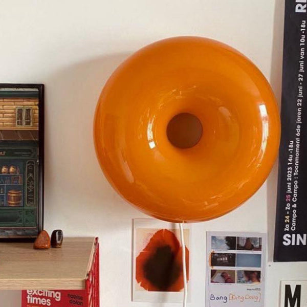 Orange donut-shaped object on a wall with posters and a painting below
