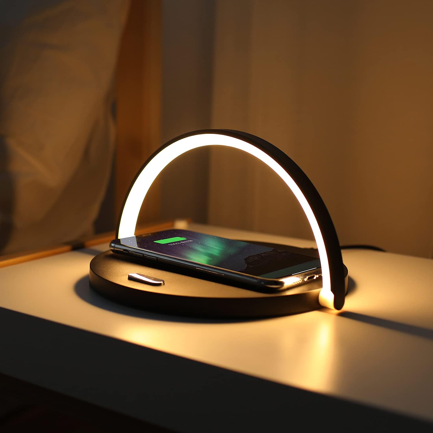 Wireless charging pad with a phone on a nightstand, illuminated by a warm light.