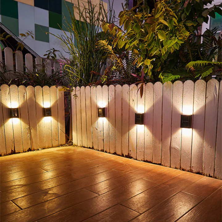 Wooden fence with wall-mounted lights casting a warm glow on a wooden deck.