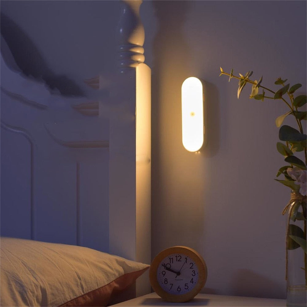 Wall-mounted light fixture casting a warm glow in a bedroom setting with an alarm clock and plant.