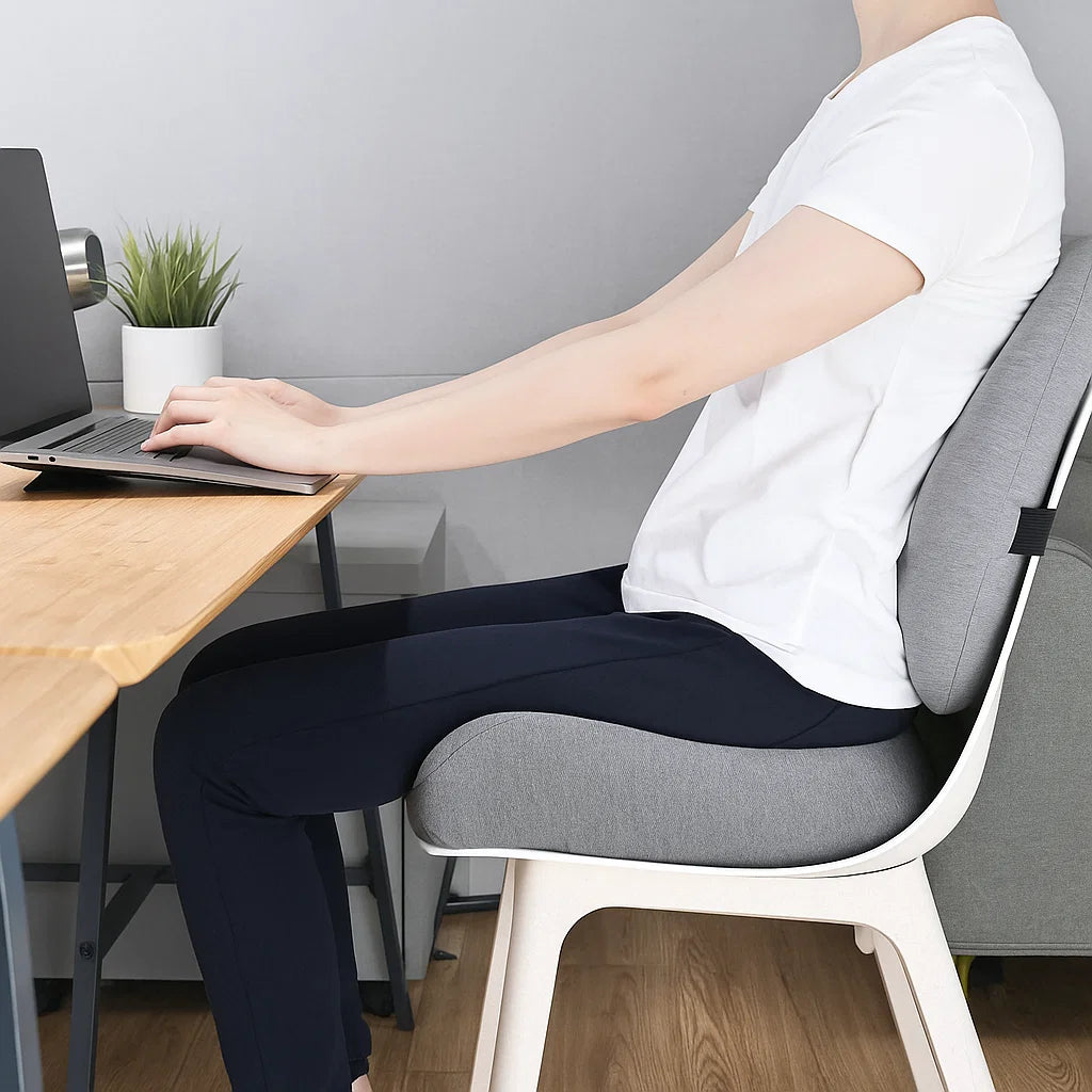 Person sitting at a desk with a laptop, using a gray cushion on their chair.