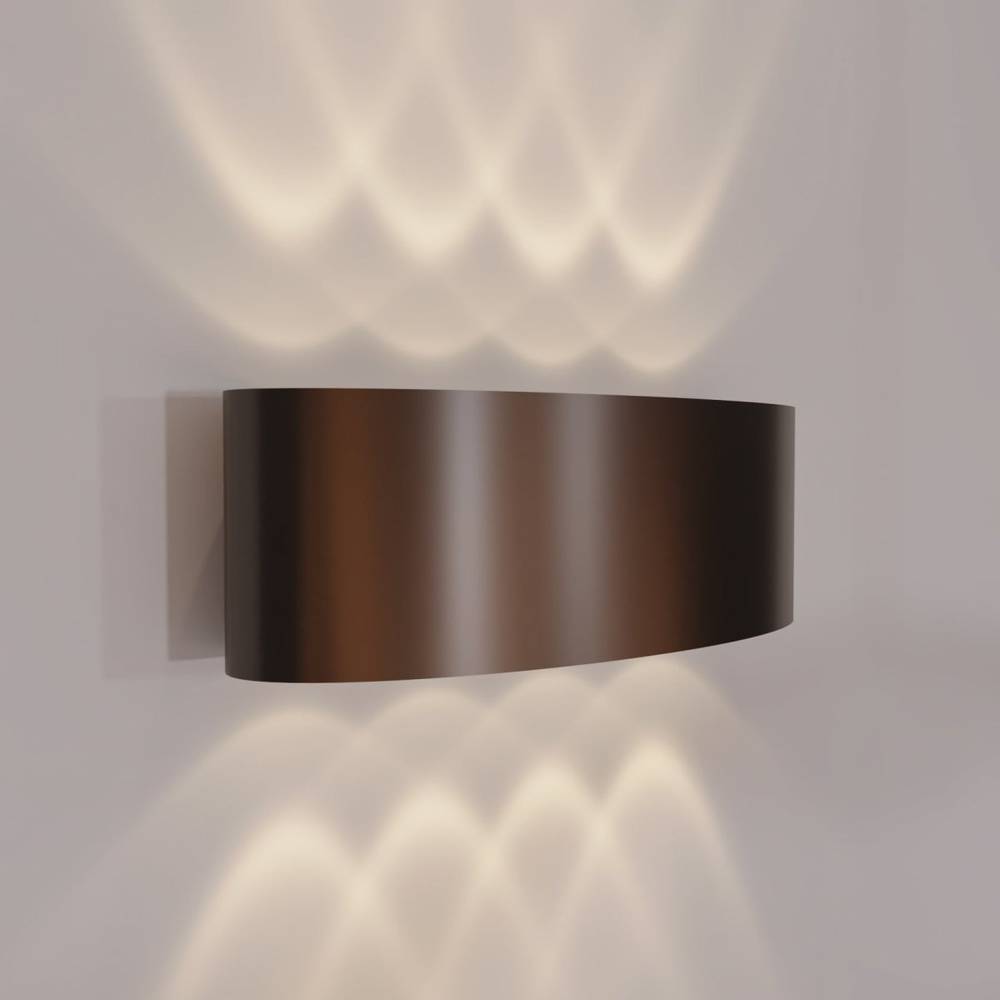 Wall-mounted bronze light fixture casting shadows on a gray wall